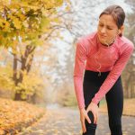Kontuzja - kobieta biegająca po parku trzymająca się za bolące kolano.
